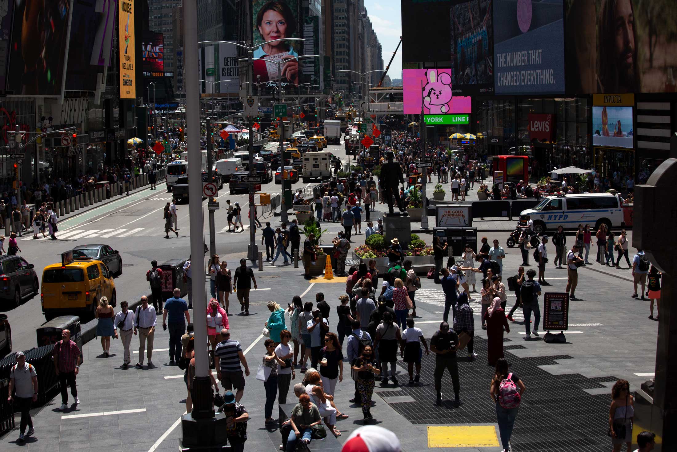 Crowds of people and traffic move through Times Square on a sunny day.